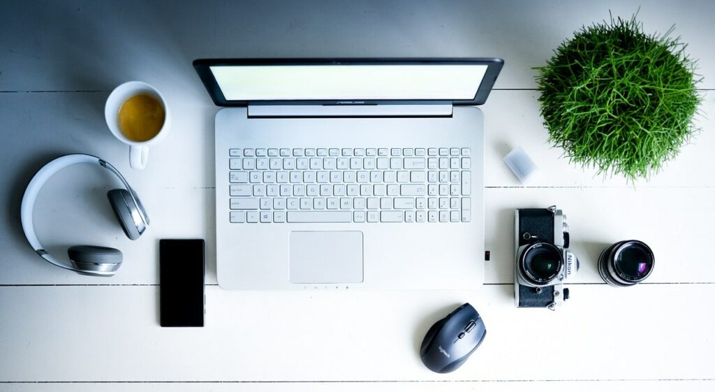 Photograph of a desktop with a laptop, headphones, coffee, a plant, and other office supplies on it.