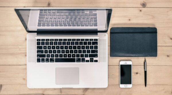 Tidy desk with laptop, smartphone, day planner, and pen neatly arranged.