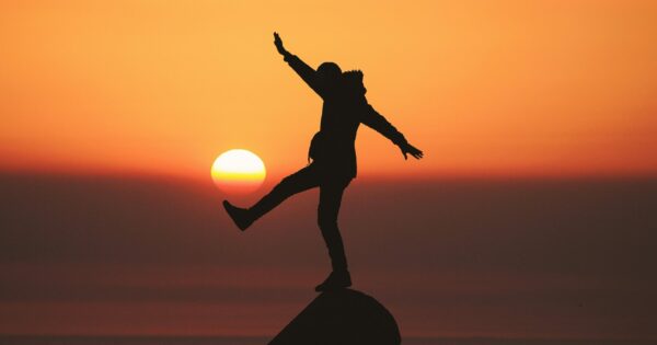Silhouette of person balanced on rock against a sunset.