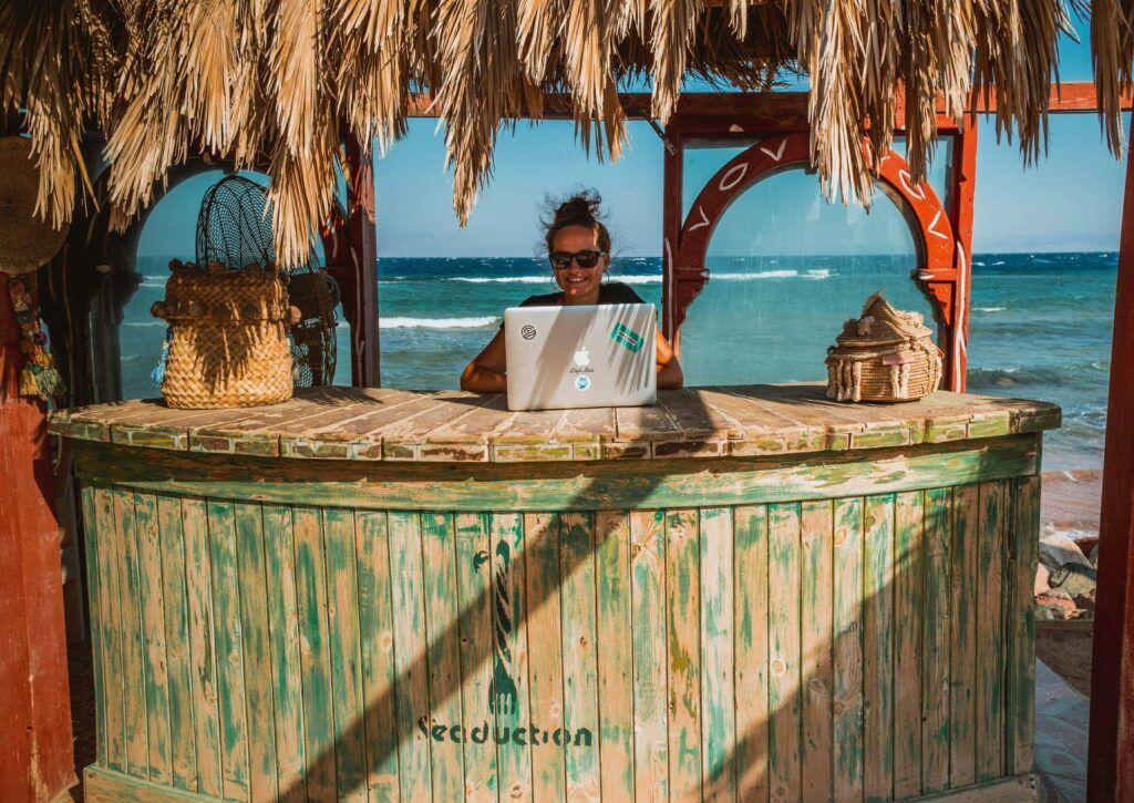 Smiling woman working on laptop at beach.