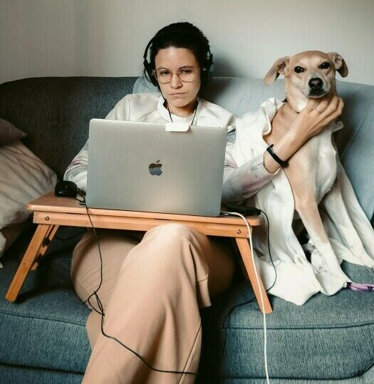 Woman on sofa with dog working on laptop. Not smiling.